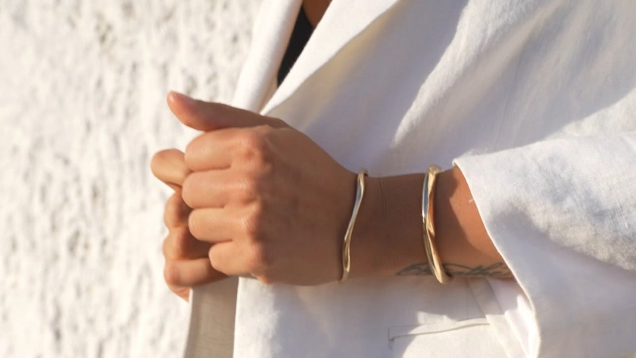 Person wearing a white blazer and dark pants with gold bracelets on a light background